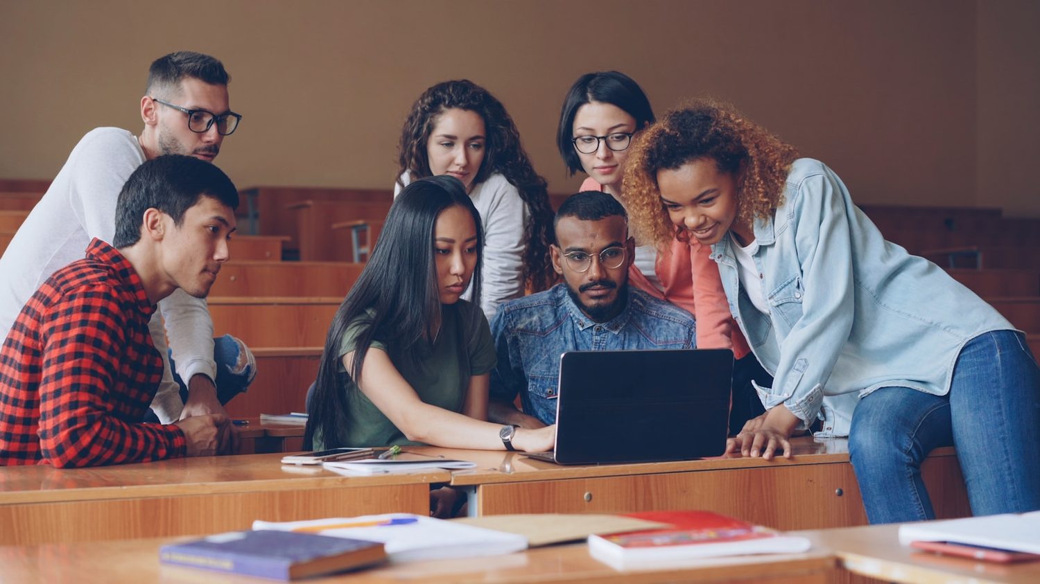 Students gathered around a laptop in a lecture theatre