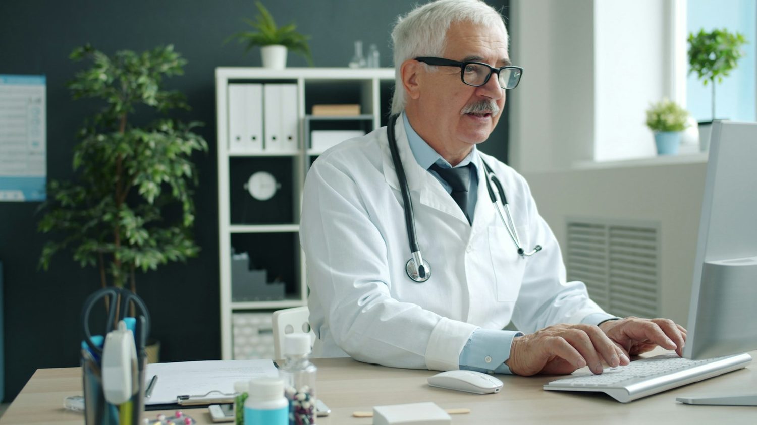 A doctor working at a computer in a consulting room